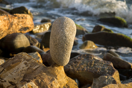 Balanced stone on the seashore summertime and sea waves background at the sunset closeup