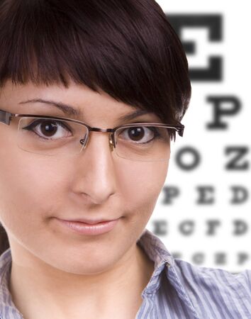 Beautiful young woman wears trendy glasses. Eye chart in background.の写真素材