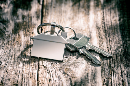 House key on a house shaped keychain on wooden table. Concept for real estate or renting home.の写真素材