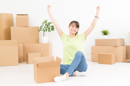 Young happy woman, a student, moved into a new apartment. Unpacks boxes in the new house. She raised her hands up as a sign of success.の写真素材