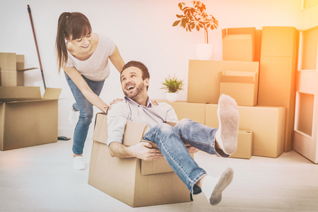 Young couple people have fun while moving to a new apartment. Boy pushes box with the girl. Happy people in the new house.の写真素材