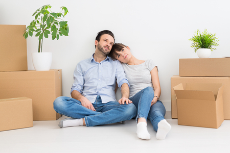 A young couple sitting on the floor and looking up. Dream and enjoy your new home.の写真素材