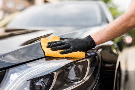 Car detailing - the man holds the microfiber in hand and polishes the car. Selective focus.の写真素材