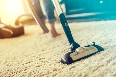 Young woman using a vacuum cleaner while cleaning carpet in the house.