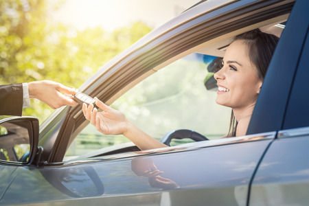 A young beautiful woman receive the keys to the new car from the dealer.の写真素材