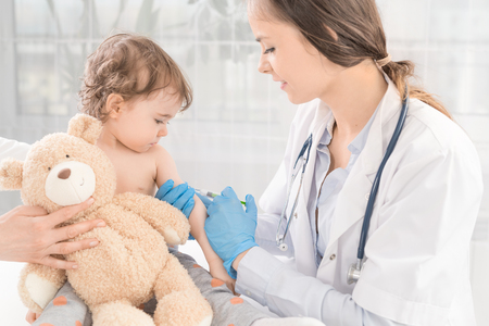 Young woman pediatrician performs a vaccination of a little girl. The girl is holding a mascot.の写真素材