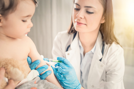 Young woman pediatrician performs a vaccination of a little girl. The girl is holding a mascot.の写真素材