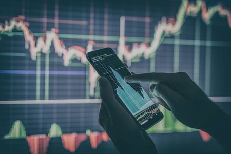 Businessman checking stock market data. He using a mobile phone. Analysis economy data on forex earn graph.の写真素材