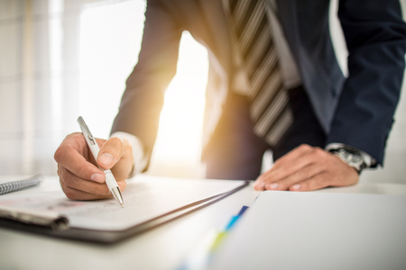 Business man signing contract document on office desk, making a deal.