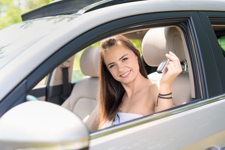 A young beautiful woman receive the keys to the new car from the dealer.の写真素材