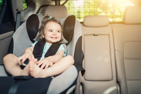 Beautyful smiling baby girl fastened with security belt in safety car seatの写真素材