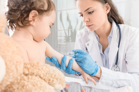 Young woman pediatrician performs a vaccination of a little girl. The girl is holding a mascot.の写真素材