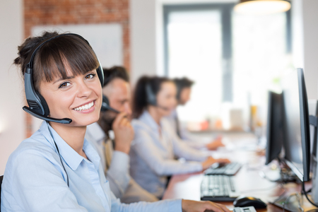 Call center worker accompanied by her team. Smiling customer support operator at work. Young employee working with a headset.の写真素材
