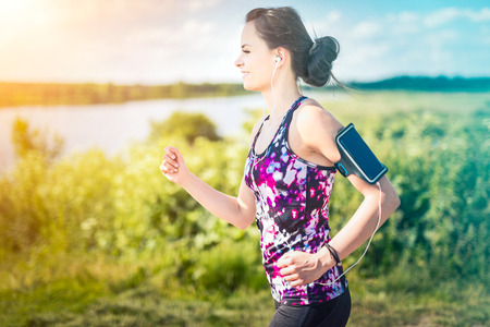 Beautiful, young woman running on the water's edge by the country road. Jogging concept.