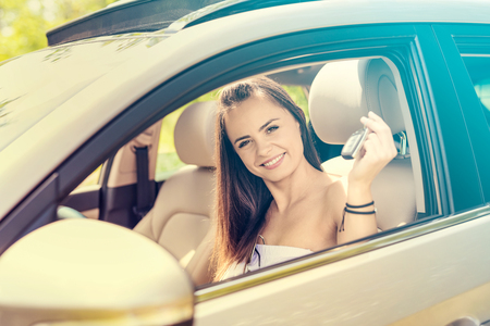 A young beautiful woman receive the keys to the new car from the dealer.の写真素材