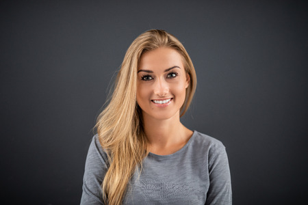 Beautiful cute cheerful girl standing over dark grey background and looking on camera. Portrait woman concept.の写真素材