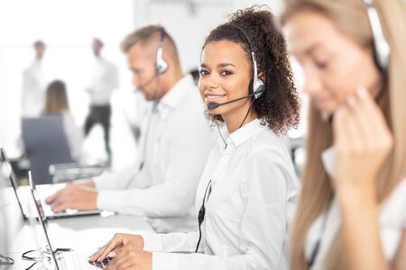 Call center worker accompanied by her team. Smiling customer support operator at work. Young employee working with a headset.の写真素材