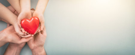 An adult, mother, father and child hold a red heart in their hands. Concept for charity, health...