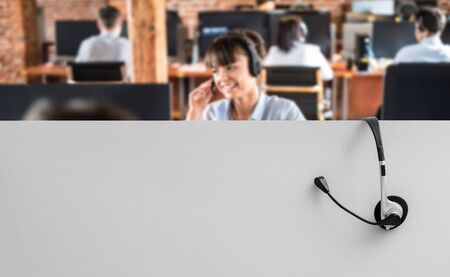 Call center worker accompanied by her team. Smiling customer support operator at work. Young employee working with a headset.の写真素材