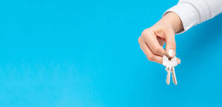 Female hand holding and giving house key on copy space background. Real estate agent.の写真素材