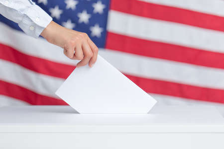 The voter holds his vote ballot paper and places it in the ballot box. Filling in ballots and casting votes in booths at polling station. The concept of free democratic vote elections.の写真素材