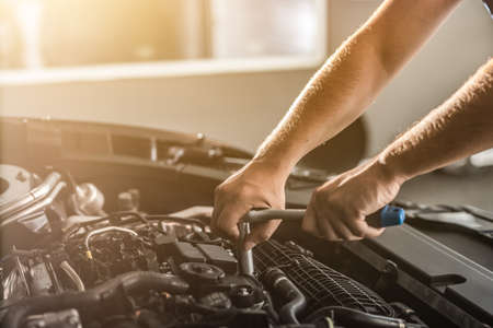 Auto mechanic working and repair on car engine in mechanics garage. Car service. Man with wrench at workshop.の写真素材