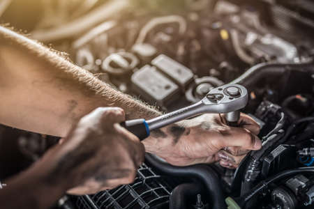 Auto mechanic working and repair on car engine in mechanics garage. Car service. Man with wrench at workshop.の写真素材