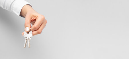 Female hand holding and giving house key on copy space background. Real estate agent.の写真素材