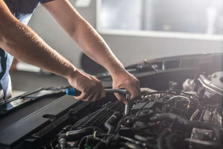 Auto mechanic working and repair on car engine in mechanics garage. Car service. Man with wrench at workshop.の写真素材