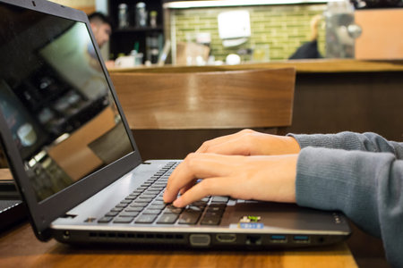 Hand of Asian woman student working on a laptop at a coffee shop