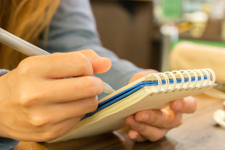 female hands with pen writing on notebook at coffee shopの写真素材