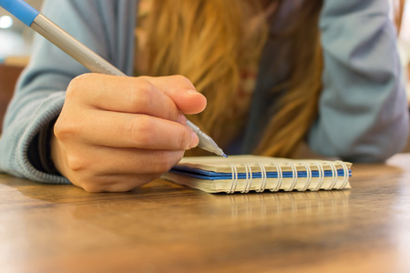 female hands with pen writing on notebook at coffee shopの写真素材