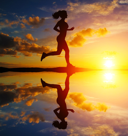 Girl running at sunset with reflection in waterの写真素材