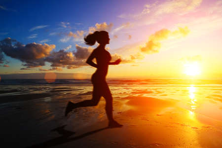Girl running at sunset with reflection in waterの写真素材