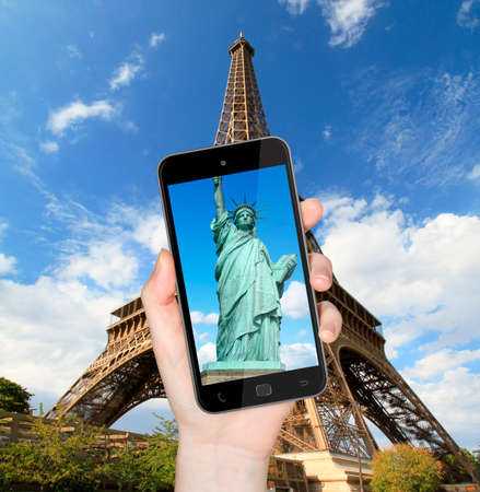 Hand taking a picture with mobile phone of the eiffel tower with statue of liberty on the screenの写真素材