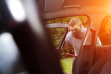 Thief wearing black clothes and leather coat stealing a carの写真素材