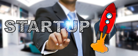 Businessman on blurred background touching hand drawn startup text and red rocket with his finger