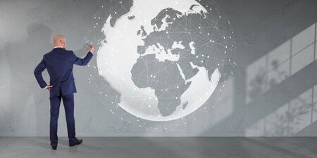 Businessman in modern interior using digital planet earth interface on a wall 3D renderingの写真素材