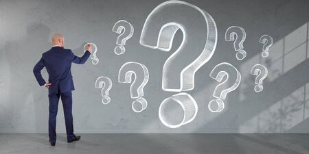 Businessman in modern interior drawing question marks sketch on a wall 3D renderingの写真素材