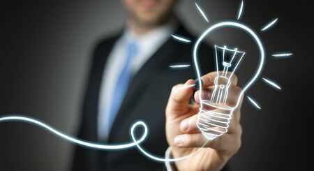 Businessman on blurred background drawing a sketch lightbulb with a penの写真素材