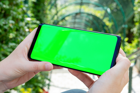 Woman holding modern smartphone in a park mockupの写真素材