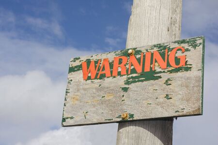 Old Wooden Warning Sign with blue sky and clouds backgroundの写真素材