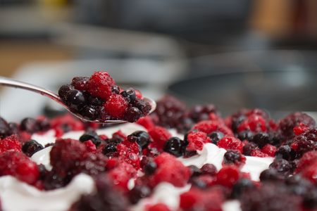 Decorating a cream cake icing with blueberries and raspberries in kitchenの写真素材