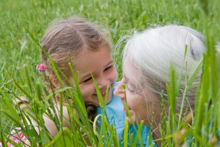 Girl laughing with her grandmother as they lie in long green grassの写真素材