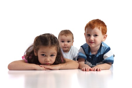 Three kids lying on floor facing camera. Isolated white background, foreground reflection.の写真素材