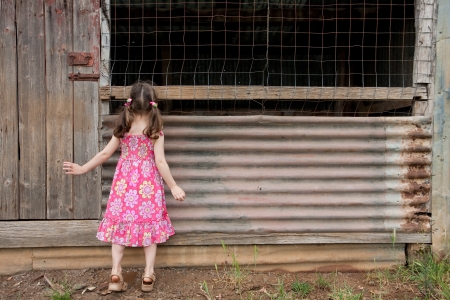 Young inquisitive girl peering into old shed on tiptoes の写真素材