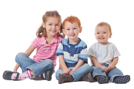 Three kids smiling and sitting on the groundの写真素材