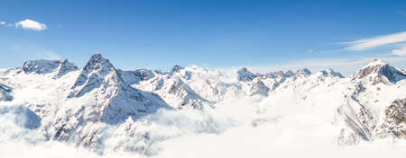 Panorama of mountains above the clouds under a clear sky on a sunny dayの写真素材