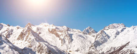 Panorama of winter snowy mountains in Caucasus region in Russia with bright sun on backgroundの写真素材