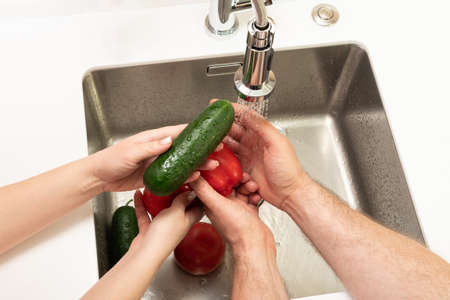 man and woman washing vegetables in the kitchen over the sinkの写真素材